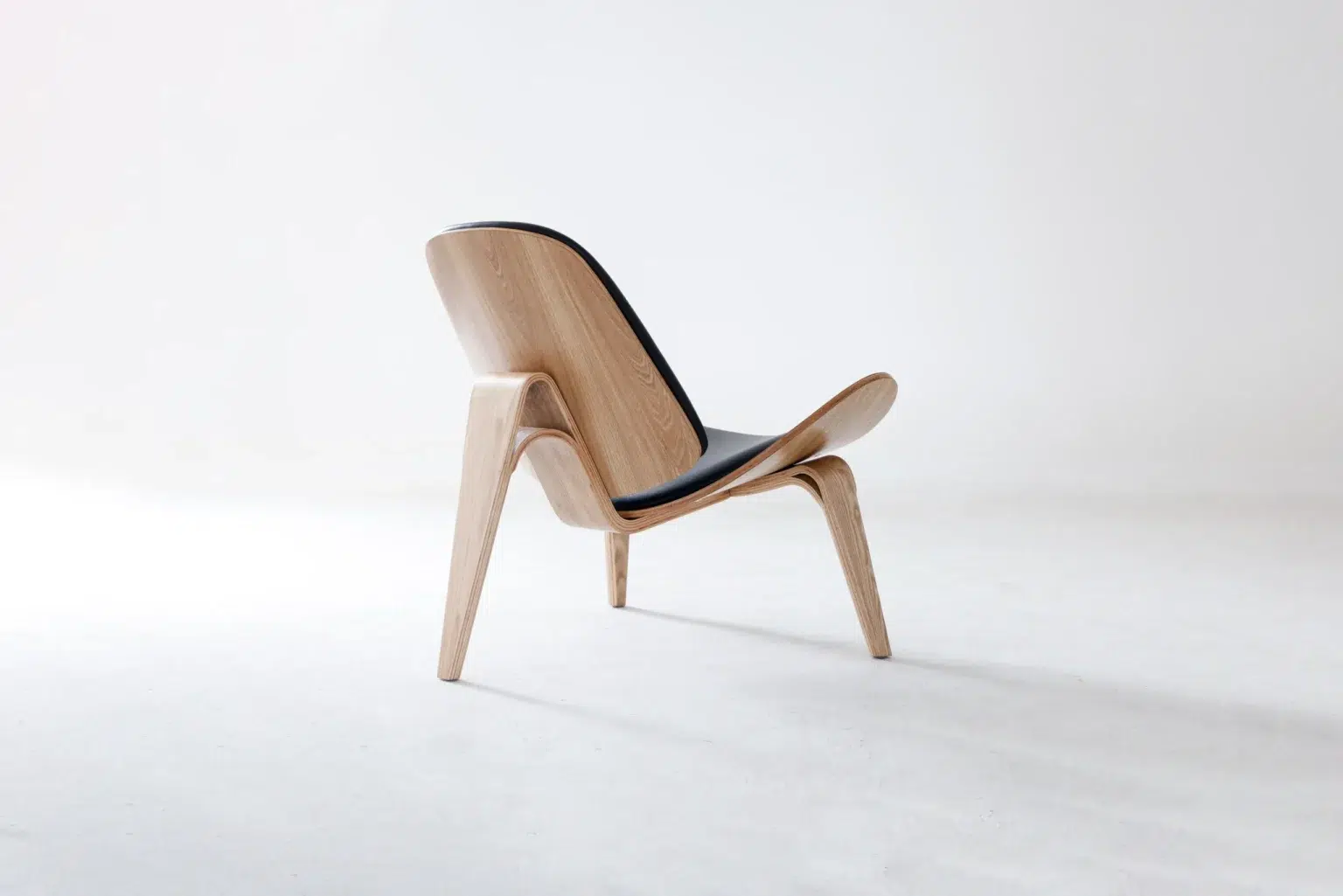 Back side view A modern wooden lounge chair with curved legs and a black cushioned seat and backrest, set against a plain white background.