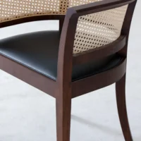 A wooden chair with a curved cane backrest and a black cushioned seat, shown on a light-coloured floor.