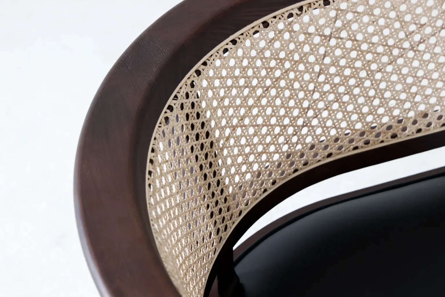 Detail display3 Close-up of a chair with a dark wood frame and a curved backrest featuring a woven cane pattern. The seat appears to be solid and black, contrasting with the light-coloured cane.