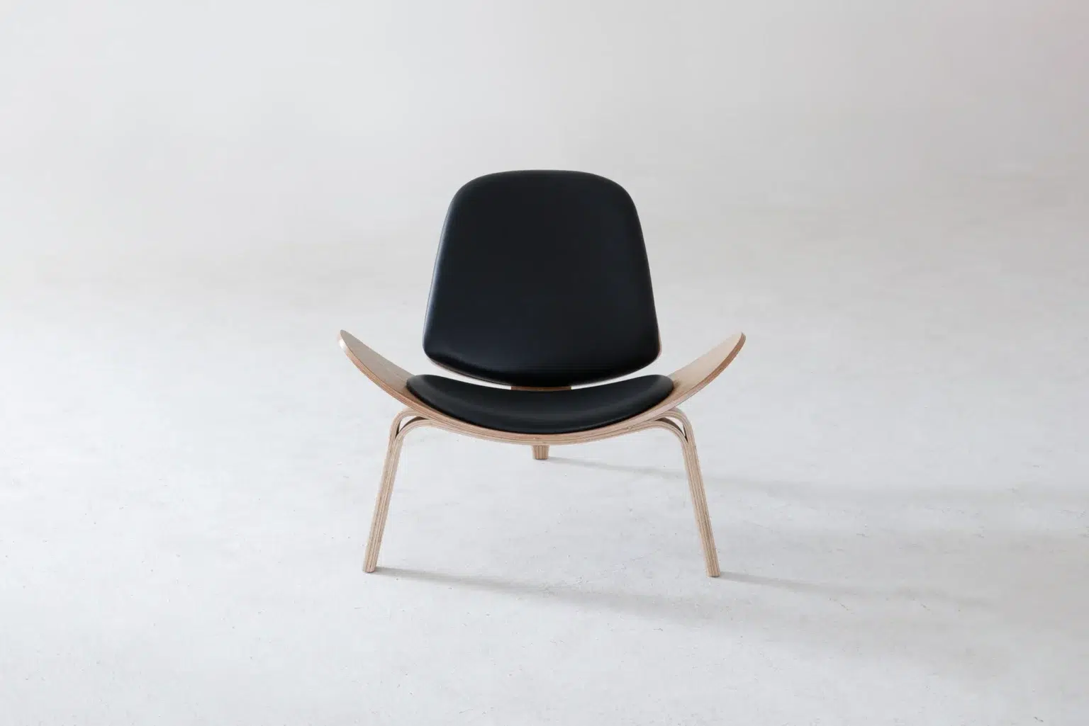 Front view A modern black lounge chair with wooden legs and a curved seat, photographed against a plain light grey background.