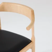 A close-up of a modern wooden chair with a curved backrest and a black cushioned seat, set against a plain white background.