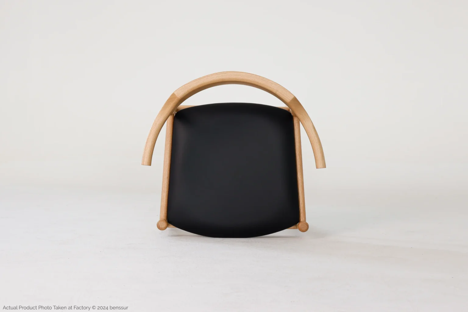 Hans Wegner_Final Chair_Replica_Microfiber_Natural_Ash_Top A modern chair with a curved wooden frame and a black cushioned seat, set against a plain white background.