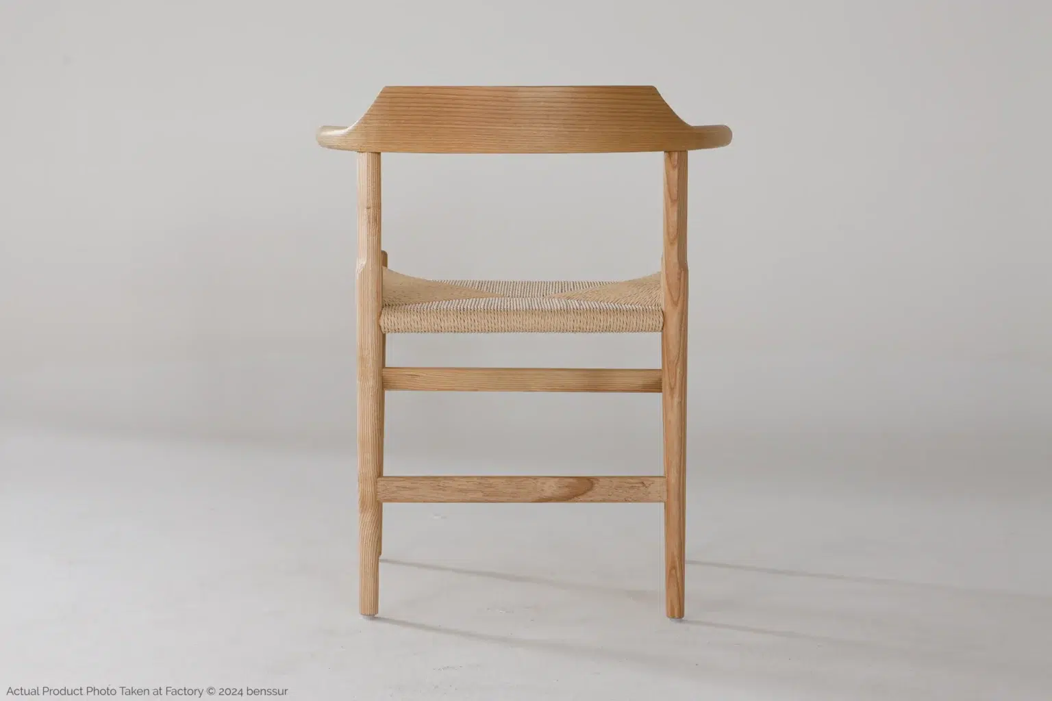 Hans Wegner_Final Chair_Replica_Paper Rope_Natural_Ash_Back A minimalist wooden chair with a curved backrest and woven seat, set against a plain light background. The chair has clean lines and a natural finish.