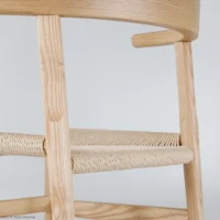 Close-up of a light wooden chair with a woven seat and smooth, rounded edges, shown against a plain, light background. The craftsmanship and texture of the materials are clearly visible.