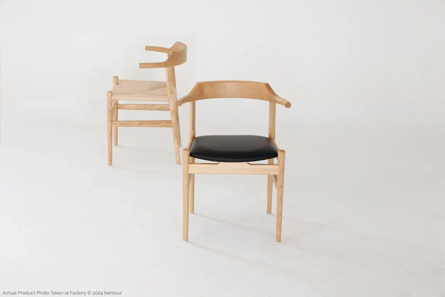 Hans Wegner_Final Chair_Replica_Paper Rope_Natural_Ash_Detail_6 Two modern wooden chairs with curved backrests are shown on a white background. One chair has a black cushioned seat, and the other has a woven seat. Both chairs feature minimalist, Scandinavian-style design.