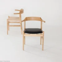Two modern wooden chairs with curved backrests are shown on a white background. One chair has a black cushioned seat, and the other has a woven seat. Both chairs feature minimalist, Scandinavian-style design.