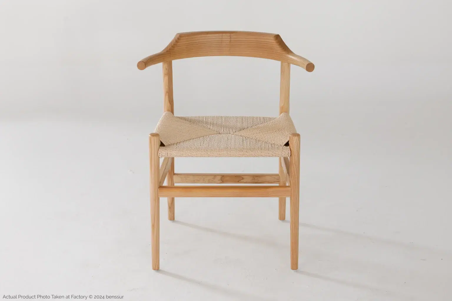 Hans Wegner_Final Chair_Replica_Paper Rope_Natural_Ash_Front A minimalist wooden chair with a curved backrest and woven seat, shown against a plain white background. The chair has simple, clean lines and light wood tones.