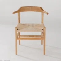 A minimalist wooden chair with a curved backrest and woven seat, shown against a plain white background. The chair has simple, clean lines and light wood tones.