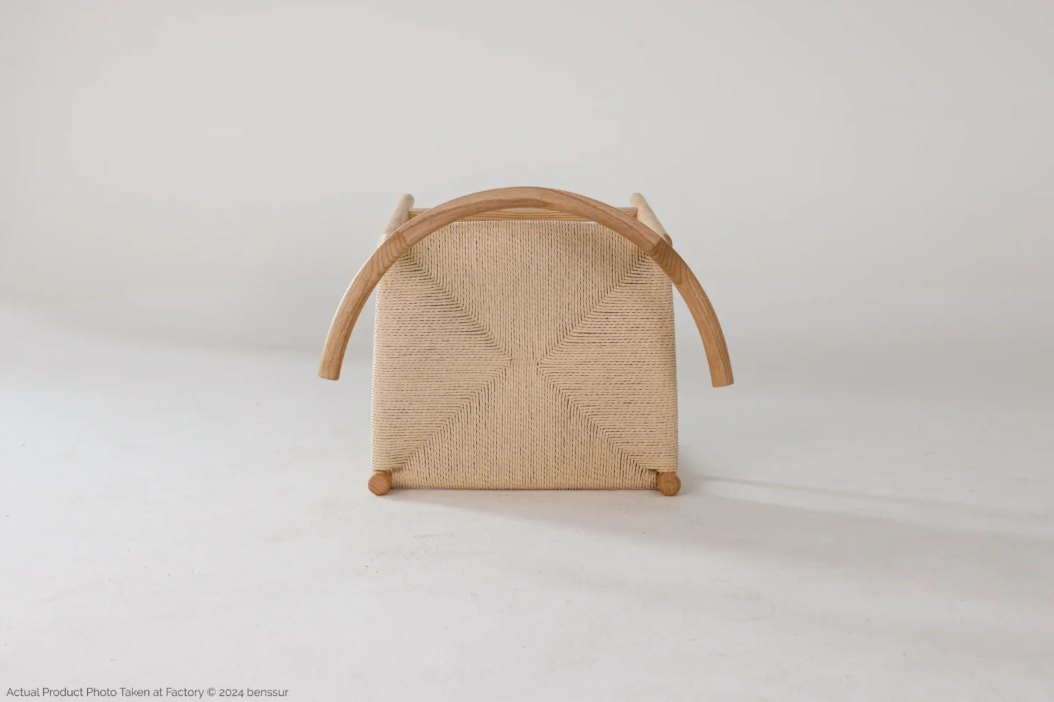 Hans Wegner_Final Chair_Replica_Paper Rope_Natural_Ash_Top A minimalist wooden chair with woven seat, seen from the front. The chair has a light wood frame and arched arms, set against a plain white background.