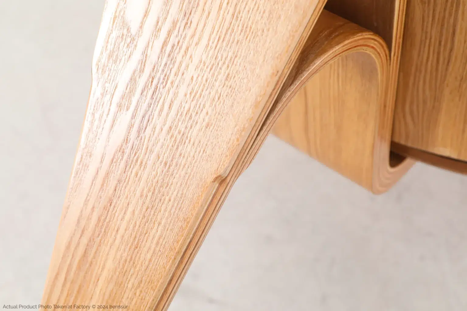 Hans Wegner_Shell Chair_Replica_Microfiber Leather_Natural_Plywood_Detail_1 Close-up of light-coloured wood with a smooth, curved, and polished surface, showing natural grain patterns and craftsmanship in the bent design against a neutral background.