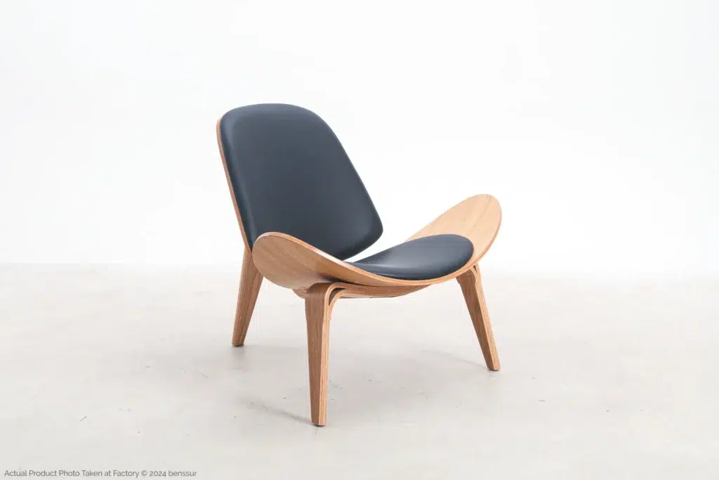 A modern wooden lounge chair with three legs, curved plywood frame, and black cushioned seat and backrest, set against a plain white background.