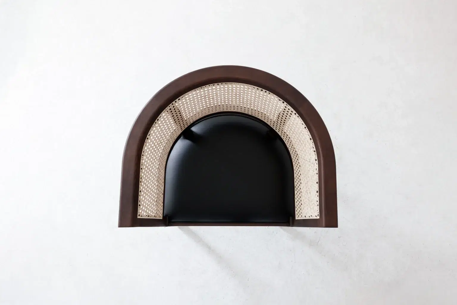 Top view A top-down view of a modern chair with a curved brown wooden frame, beige cane backrest, and black cushioned seat against a light grey background.