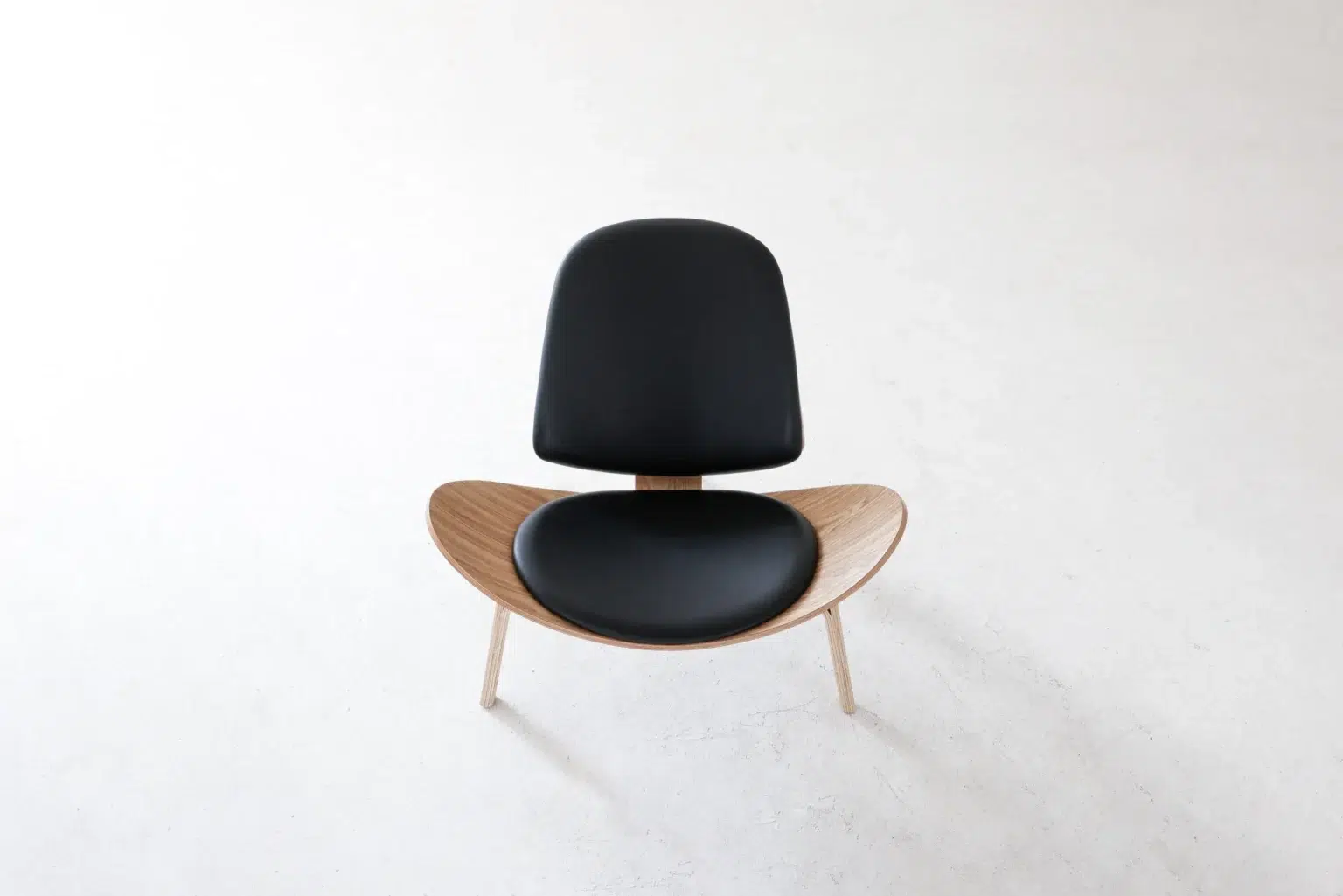 Top view A modern chair with a curved wooden seat, light wooden legs, and black cushioned backrest and seat, photographed from above on a plain white background.