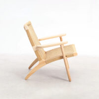 A modern lounge chair with a light wooden frame and woven natural fibre seat and backrest, shown in profile against a plain white background.