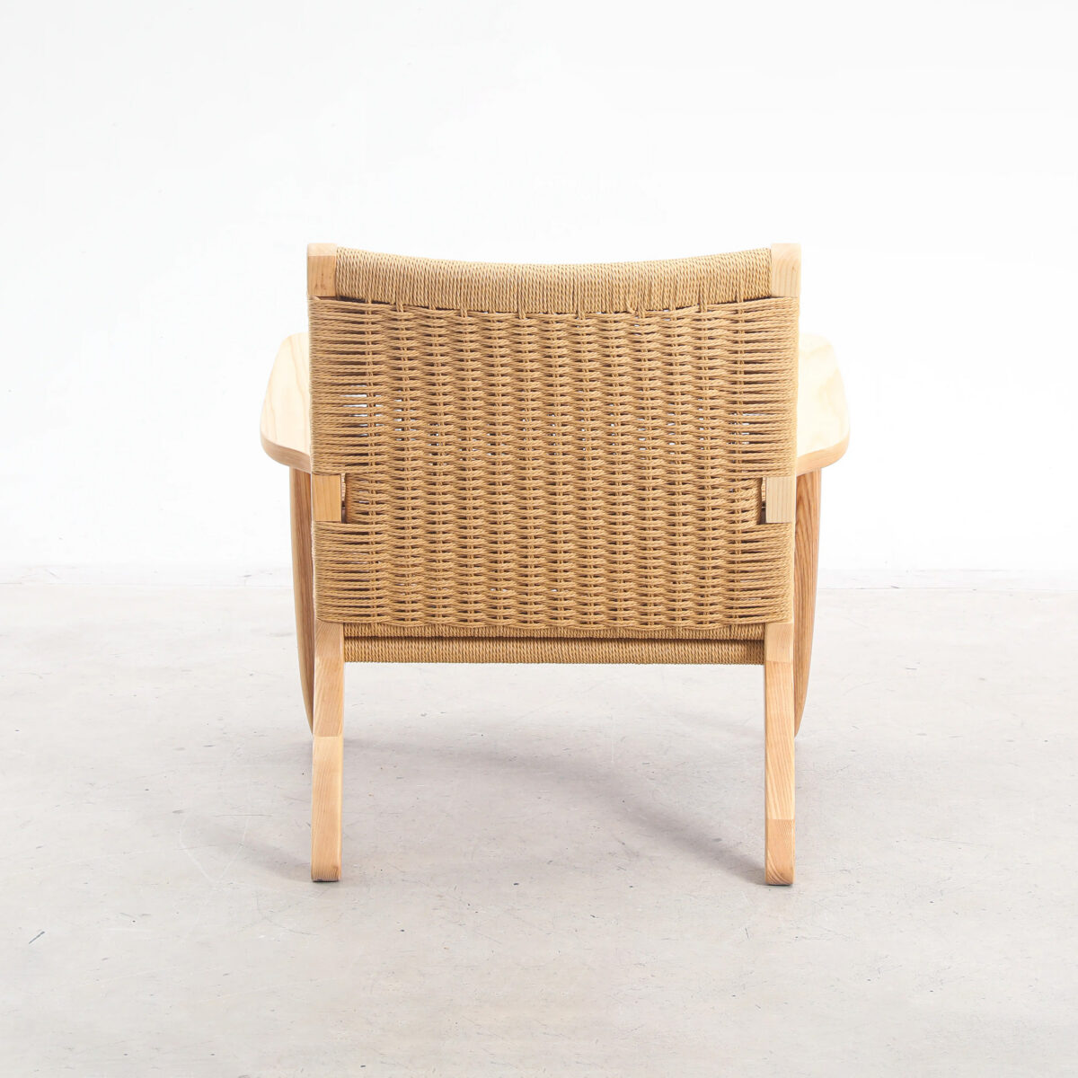Easy Chair_B2 A wooden chair with curved arms and a woven rattan backrest, viewed from behind, placed on a light-coloured floor against a plain white background.