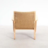 A wooden chair with curved arms and a woven rattan backrest, viewed from behind, placed on a light-coloured floor against a plain white background.