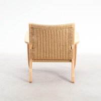 A wooden chair with curved arms and a woven rattan backrest, viewed from behind, placed on a light-coloured floor against a plain white background.