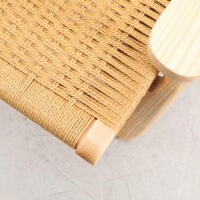 Close-up of a woven seat made of natural fibre or rope on a light wooden chair, shown from an angle above on a pale, smooth floor.