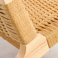 Close-up of a wooden chair with a tightly woven natural fibre seat and backrest, showcasing detailed craftsmanship and the light wood grain of the frame.