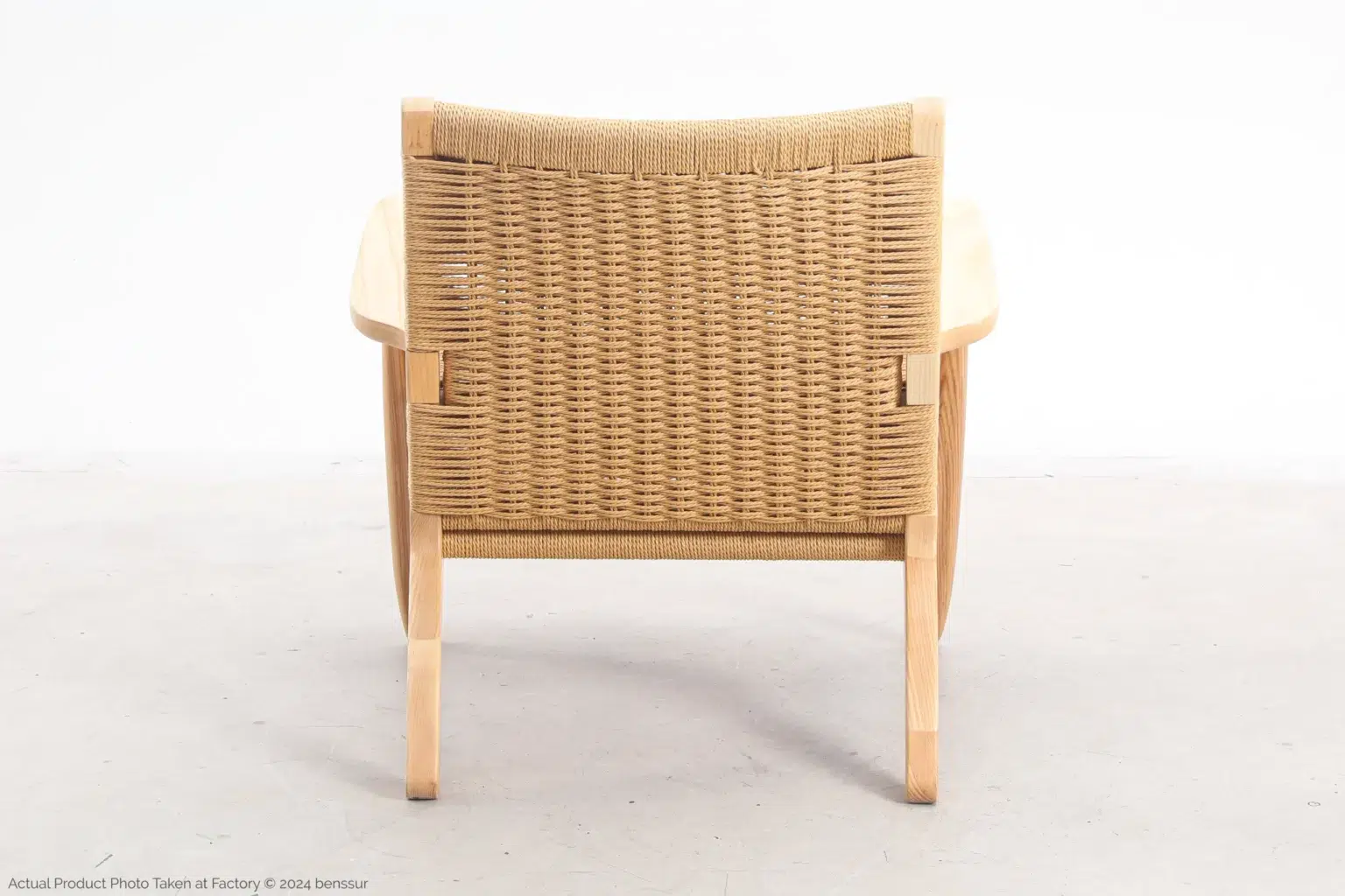 Hans Wegner_CH25 Easy Chair_Replica_Paper Rope_Natural_Ash_Back A wooden armchair with a woven backrest, viewed from behind, sits on a light-coloured floor against a plain white background.