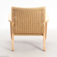 A wooden armchair with a woven backrest, viewed from behind, sits on a light-coloured floor against a plain white background.