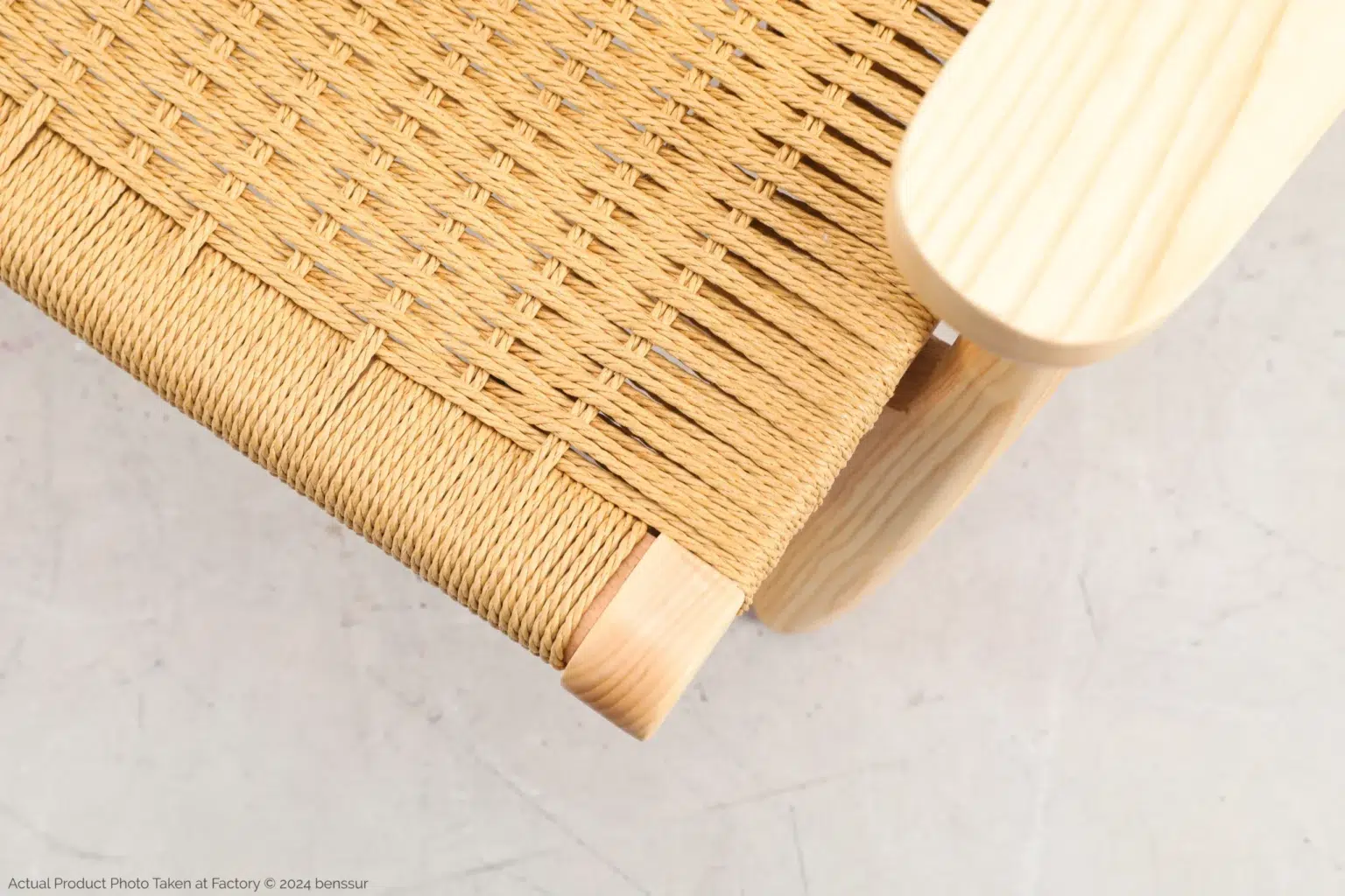 Hans Wegner_CH25 Easy Chair_Replica_Paper Rope_Natural_Ash_Detail_1 A close-up of a woven cane seat on a light wooden chair, showcasing detailed craftsmanship with tightly interlaced fibres and smooth, rounded wooden edges against a neutral background.