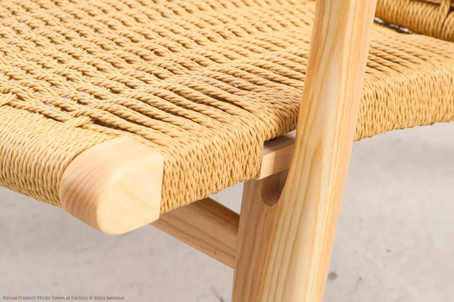 Hans Wegner_CH25 Easy Chair_Replica_Paper Rope_Natural_Ash_Detail_5 Close-up of a wooden chair’s corner, showing detailed woven cane seat and smooth, light-coloured wood frame with visible grain patterns.