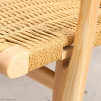 Close-up of a wooden chair’s corner, showing detailed woven cane seat and smooth, light-coloured wood frame with visible grain patterns.