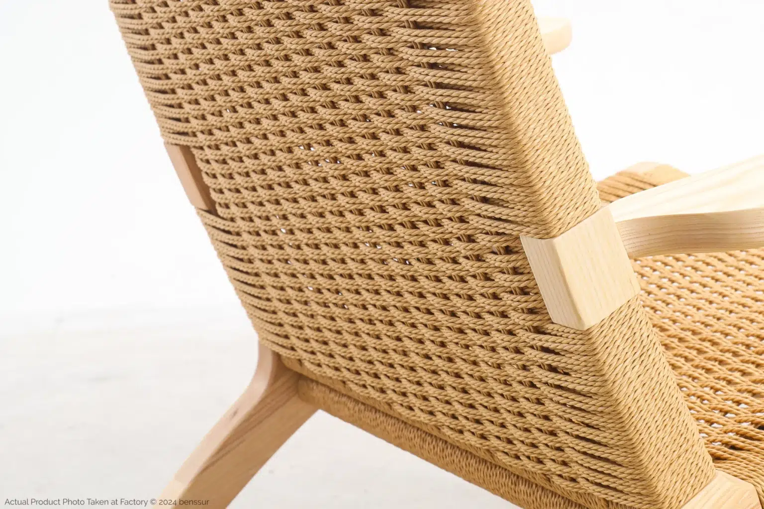 Hans Wegner_CH25 Easy Chair_Replica_Paper Rope_Natural_Ash_Detail_6 Close-up of a woven rattan chair backrest with light wooden frame and armrests against a plain, light background. The intricate weaving pattern is prominently visible.