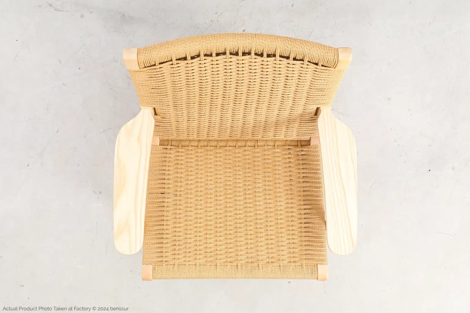 Hans Wegner_CH25 Easy Chair_Replica_Paper Rope_Natural_Ash_Top Top view of a woven rattan chair with light wooden armrests on a light-coloured floor. The chair has a natural, minimalist design and a rectangular seat and backrest.