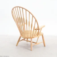 A wooden Windsor-style chair with a high, curved spindle back and flat armrests, set on a light-coloured floor against a plain white background.