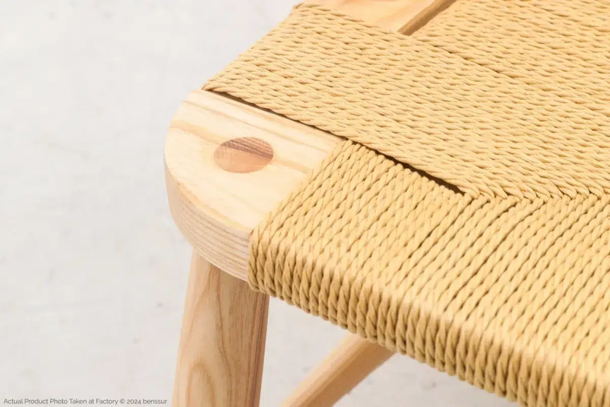 Hans Wegner_Peacock Chair_Replica_Paper Rope_Natural_Ash_Detail_2 Close-up of a wooden chair featuring light-coloured, woven rope seating and a rounded corner with visible wood grain and joinery detail. The chair has a smooth finish and a minimalist design.