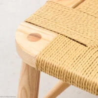 Close-up of a wooden chair featuring light-coloured, woven rope seating and a rounded corner with visible wood grain and joinery detail. The chair has a smooth finish and a minimalist design.