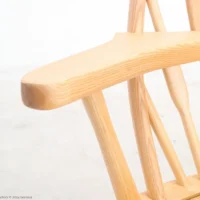Close-up of a light wooden chair with smooth curves and a natural finish, showing the armrest and part of the backrest against a plain, white background.