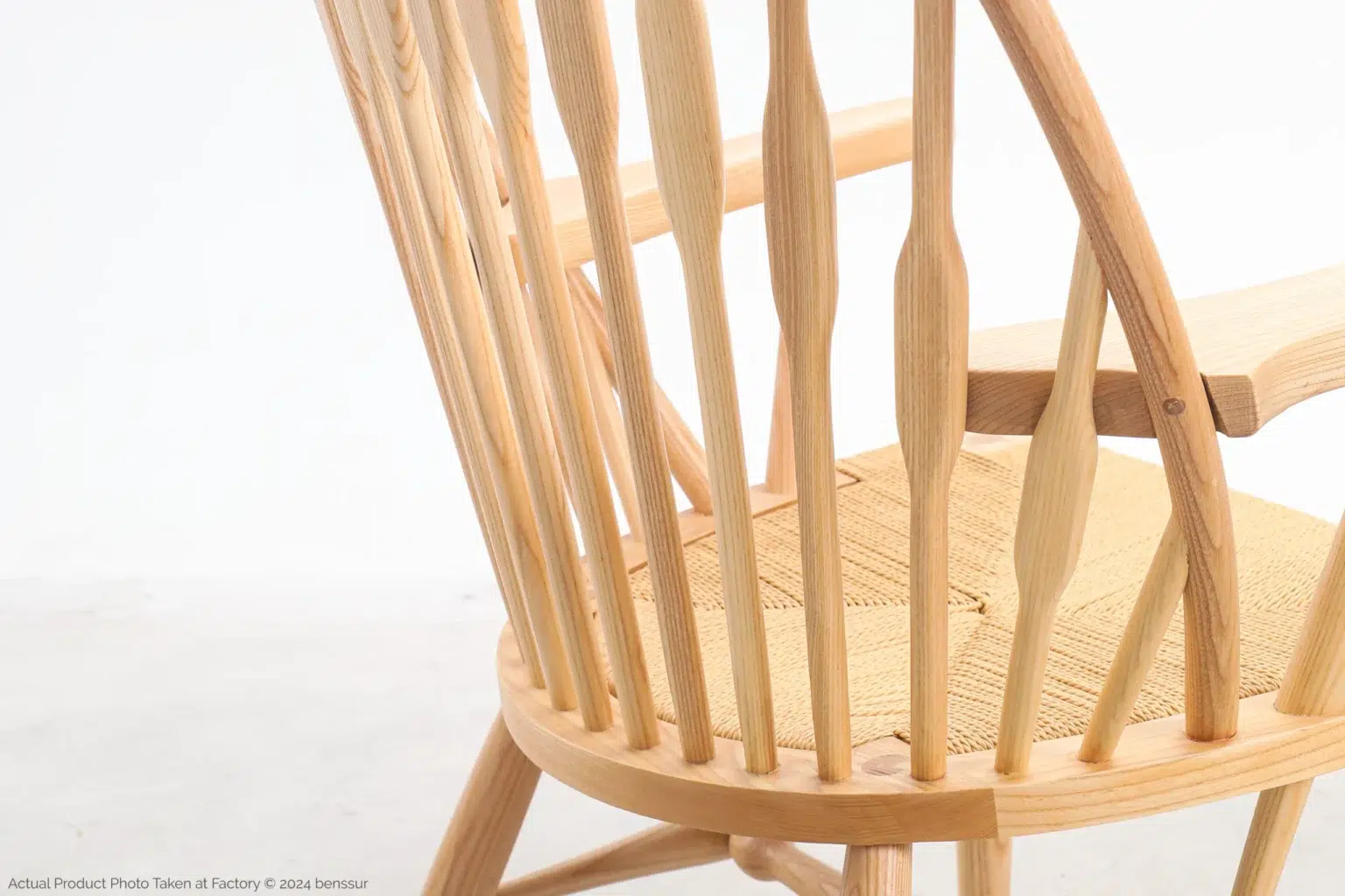 Hans Wegner_Peacock Chair_Replica_Paper Rope_Natural_Ash_Detail_5 Close-up of a light wooden chair with vertical spindle backrest, curved armrests, and a woven seat, set against a plain white background.