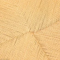 Close-up of a woven straw or wicker surface with a geometric, symmetrical pattern radiating from the centre, showcasing tightly interlaced light tan fibres.