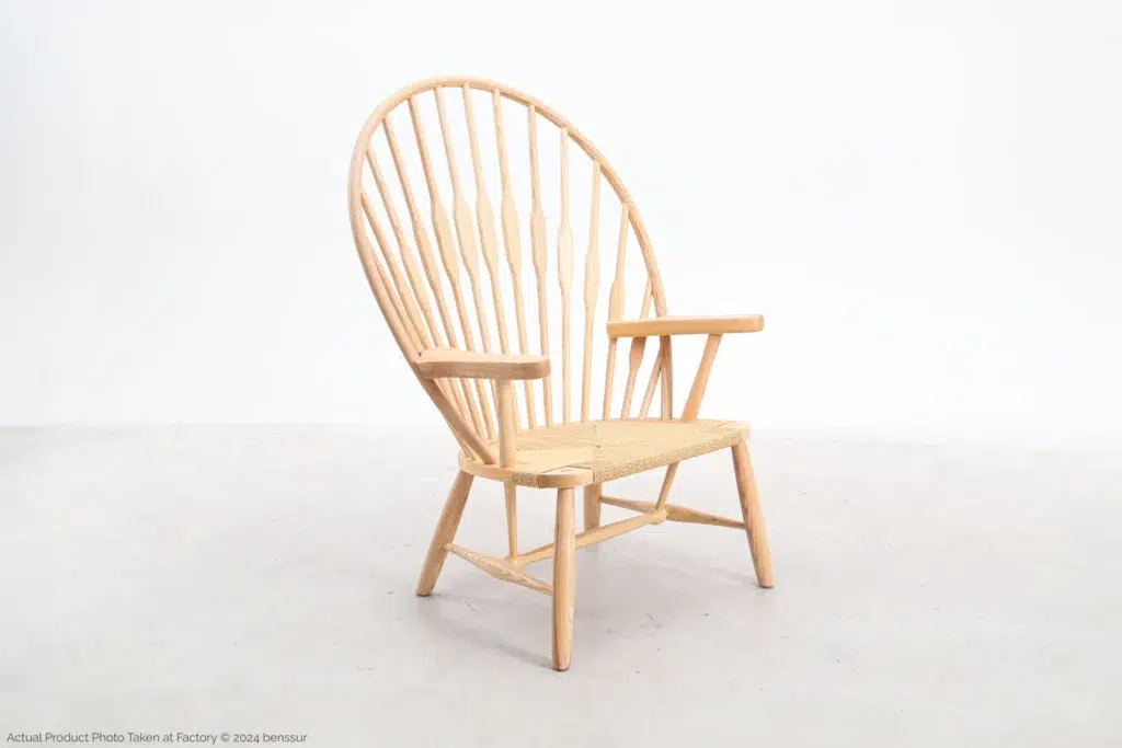 A wooden chair with a rounded, high spindle backrest, wide armrests, and a woven seat, placed on a light-coloured floor against a plain white background.