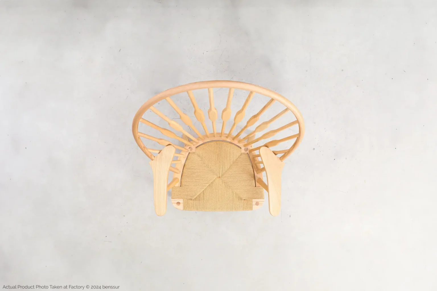 Hans Wegner_Peacock Chair_Replica_Paper Rope_Natural_Ash_Top Top-down view of a wooden chair with a rounded backrest and woven seat, positioned against a light grey background. The chair’s legs and spindles are visible from above.