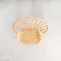 Top-down view of a wooden chair with a rounded backrest and woven seat, positioned against a light grey background. The chair’s legs and spindles are visible from above.