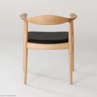 A wooden chair with a curved backrest, armrests, and a black cushioned seat is shown against a plain white background. The design is simple and modern, with smooth, light-coloured wood.