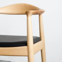 A close-up of a modern wooden chair with a curved backrest and black cushioned seat, set against a plain white background.