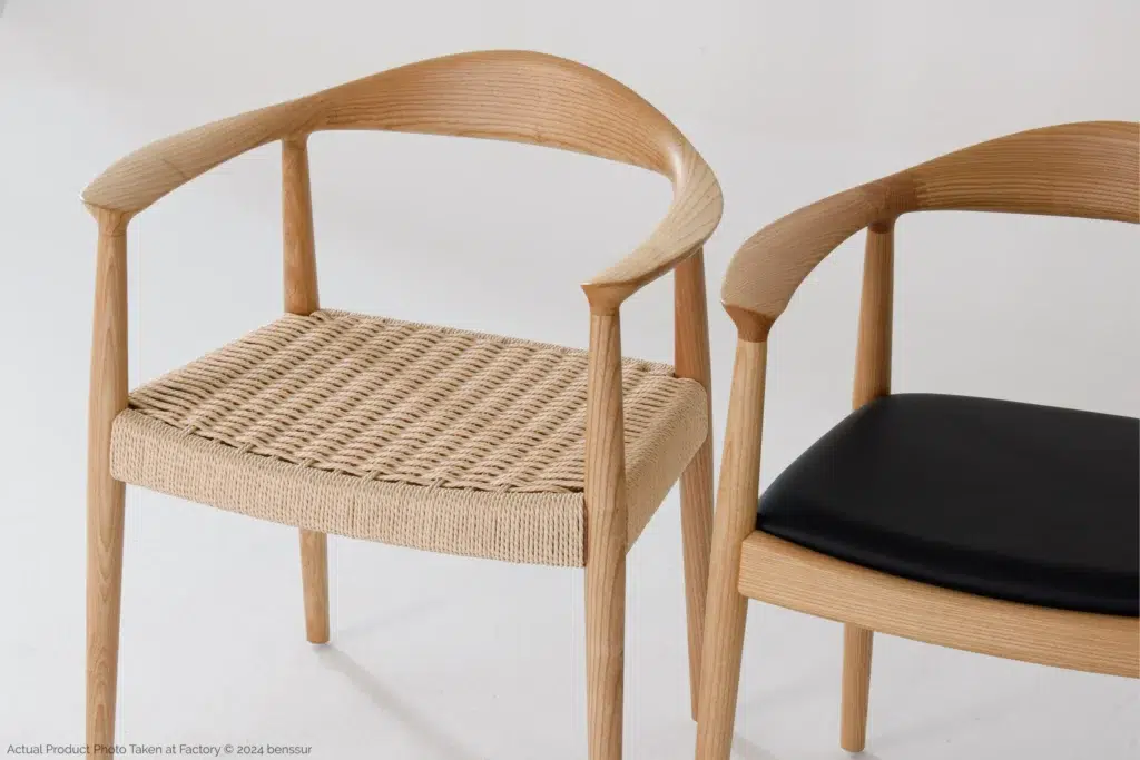 Two modern wooden chairs with curved backrests; one has a woven rattan seat, and the other has a smooth black cushioned seat, both against a plain white background.