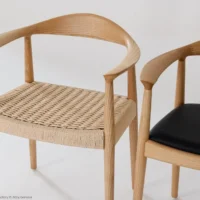 Two modern wooden chairs with curved backrests; one has a woven rattan seat, and the other has a smooth black cushioned seat, both against a plain white background.