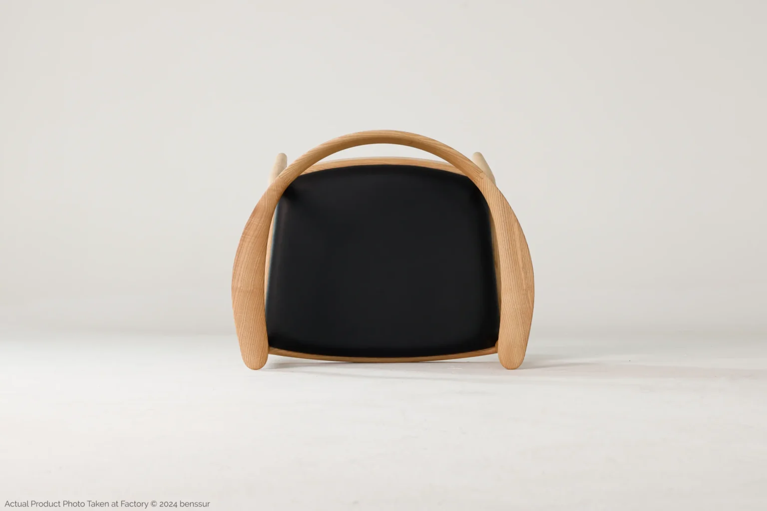 Hans Wegner_Round Chair_Replica_Microfiber_Natural_Ash_Top A modern chair with a curved wooden frame and a black cushioned seat, shown from the front against a plain white background.