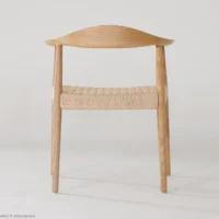 A minimalist wooden chair with a curved backrest and woven seat, photographed against a plain white background. The chair has a simple, Scandinavian-inspired design.
