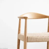 Minimalist wooden chair with a curved backrest and woven seat, set against a plain white background. The design highlights smooth, light-coloured wood and simple, elegant lines.
