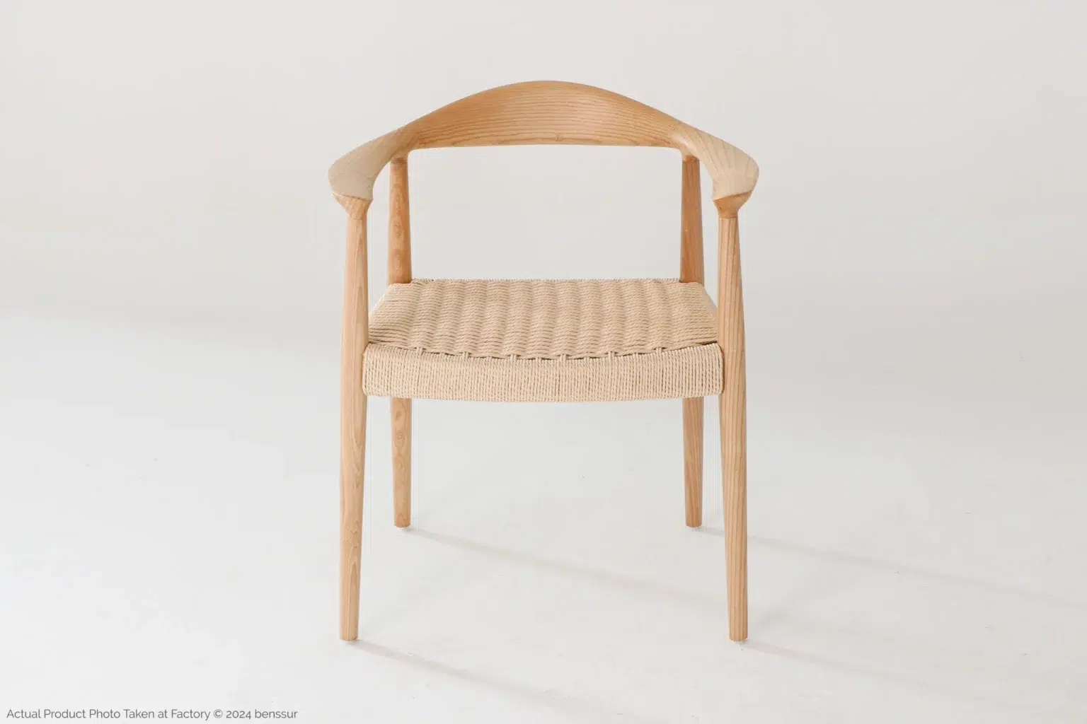 Hans Wegner_Round Chair_Replica_Paper Rope_Natural_Ash_Front A wooden chair with curved armrests and a woven seat, set against a plain white background. The design is minimalist and modern, with smooth lines and light-coloured wood.