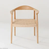 A wooden chair with curved armrests and a woven seat, set against a plain white background. The design is minimalist and modern, with smooth lines and light-coloured wood.