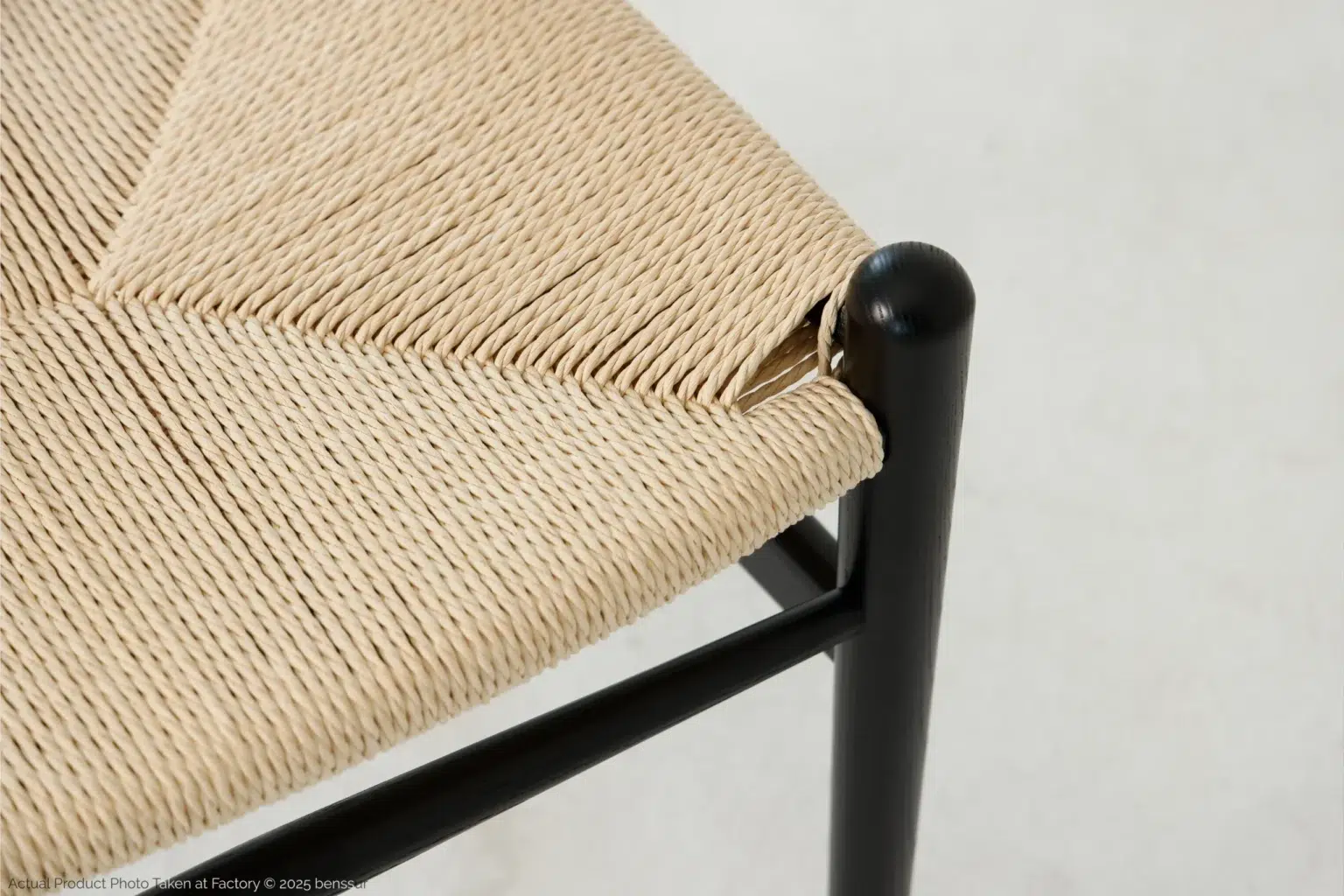 Hans Wegner_Wishbone Chair_Replica_Paper Rope_Black_Ash_Detail_1 Close-up of a woven natural-fibre seat on a black wooden chair frame, showing detailed craftsmanship and texture against a light background.