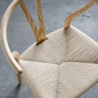 A wooden chair with a curved backrest and woven seat is placed on a grey concrete floor, viewed from above. The natural wood and intricate seat weave create a minimalist, Scandinavian design.